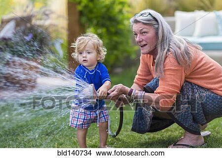 Caucasian grandmother and baby grandson watering lawn with hose View Large Photo Image Picture - Caucasian grandmother and baby grandson watering lawn with hose. Fotosearch