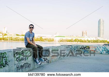 Stock Image - Caucasian man sitting on urban graffiti wall. Fotosearch