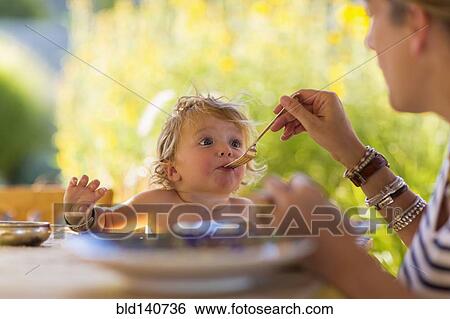 Caucasian mother feeding baby son at table View Large Photo Image Stock Photograph - Caucasian mother feeding baby son at table. Fotosearch