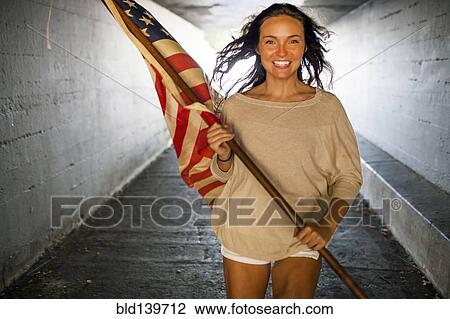 Stock Image - Caucasian woman carrying American flag in tunnel. Fotosearch