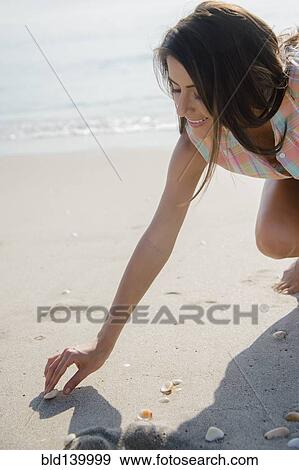 Stock Photo - Caucasian woman collecting seashells on beach. Fotosearch