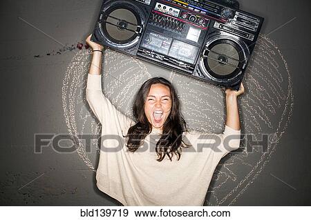 Stock Photo - Caucasian woman holding boom box near chalk heart on wall. Fotosearch