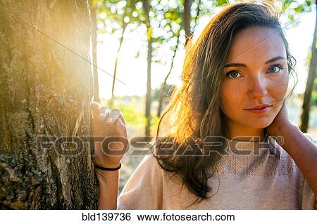 Stock Photograph - Caucasian woman leaning against tree in park. Fotosearch