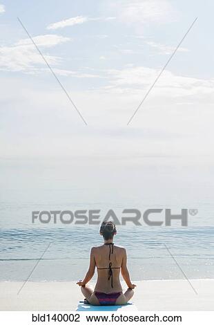 Stock Image - Caucasian woman meditating on beach. Fotosearch