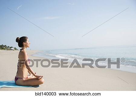 Stock Image - Caucasian woman meditating on beach. Fotosearch