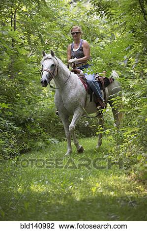 Stock Image - Caucasian woman riding horse in rural field. Fotosearch