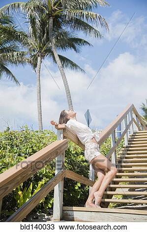 Stock Image - Caucasian woman standing on wooden staircase. Fotosearch