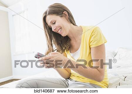 Stock Photo - Caucasian woman using cell phone on bed. Fotosearch