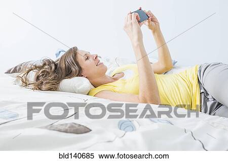 Caucasian woman using cell phone on bed View Large Photo Image Stock Photography - Caucasian woman using cell phone on bed. Fotosearch