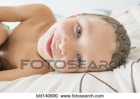 Stock Image - Close up of Caucasian boy smiling on bed. Fotosearch
