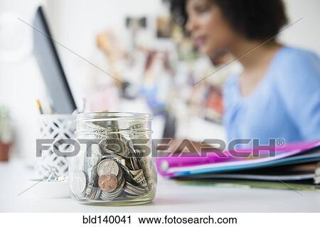 Stock Image - Close up of change jar on desk. Fotosearch