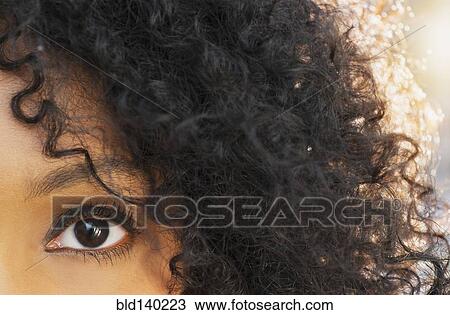 Stock Image - Close up of eye and curly hair of mixed race woman. Fotosearch