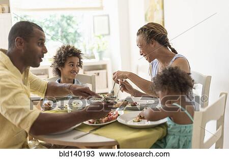 Stock Image - Family eating together at dining room table. Fotosearch