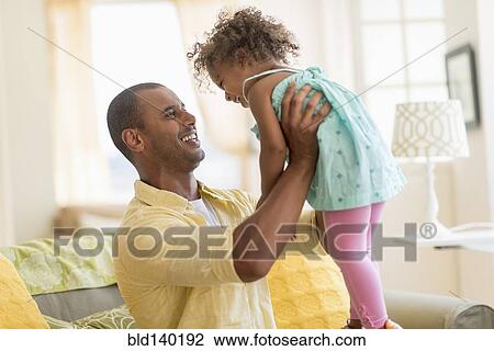 Stock Image - Father and daughter playing together in living room. Fotosearch