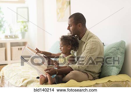 Picture - Father and daughter reading book on bed. Fotosearch