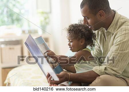 Stock Photograph - Father and daughter reading book on bed. Fotosearch