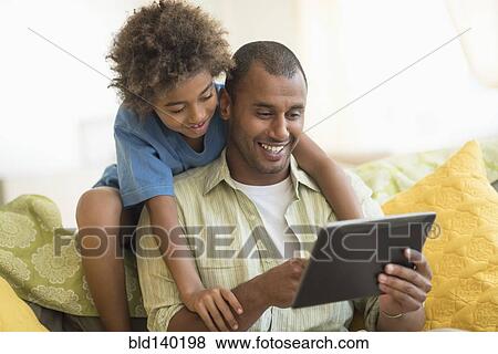 Stock Photo - Father and son using digital tablet together in living room. Fotosearch