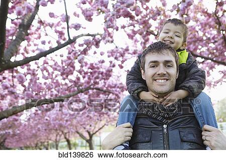 Stock Photograph - Father carrying son on shoulders in park. Fotosearch