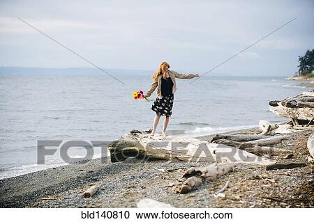 Stock Image - Girl balancing on driftwood on beach. Fotosearch