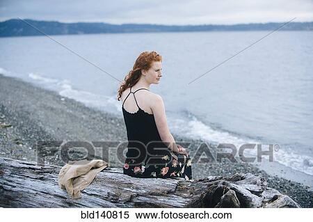 Stock Photography - Girl sitting on driftwood on beach. Fotosearch