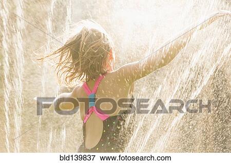 Stock Photo - Girl standing in sprinkler. Fotosearch