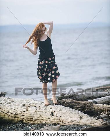 Stock Image - Girl walking on driftwood on beach. Fotosearch