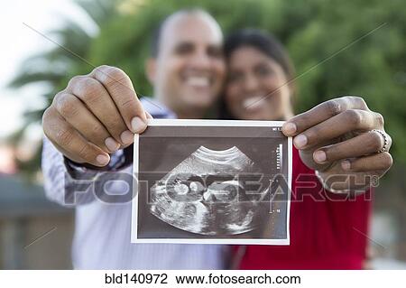 Stock Image - Happy couple holding sonogram. Fotosearch