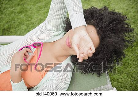 Stock Image - High angle view of woman with sunglasses covering her eyes. Fotosearch
