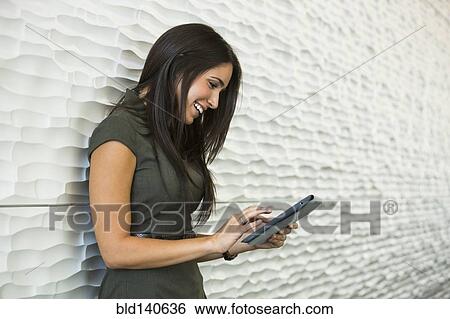 Stock Photograph - Hispanic businesswoman using digital tablet near wall. Fotosearch
