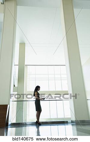 Stock Photography - Hispanic businesswoman using digital tablet in office hallway. Fotosearch