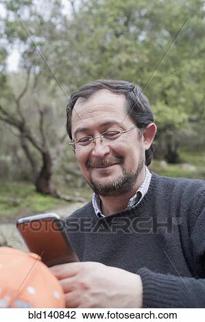 Stock Image - Hispanic man using cell phone in park. Fotosearch