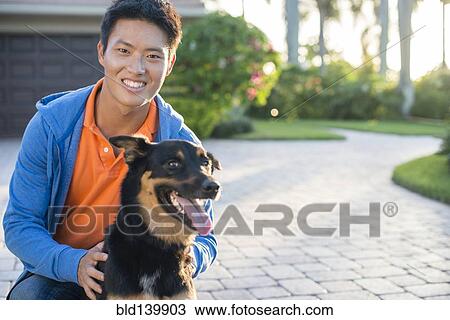 Stock Image - Korean man holding dog in driveway. Fotosearch