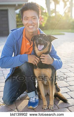 Stock Image - Korean man hugging dog in driveway. Fotosearch