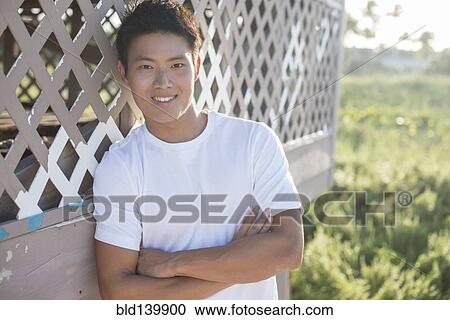 Stock Image - Korean man leaning against porch outdoors. Fotosearch