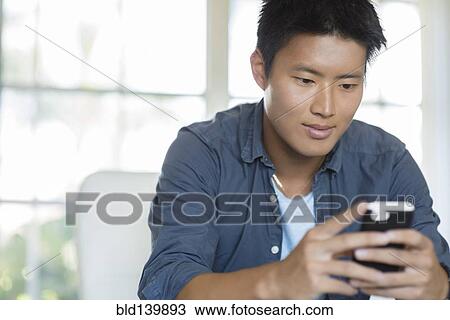 Stock Image - Korean man using cell phone indoors. Fotosearch