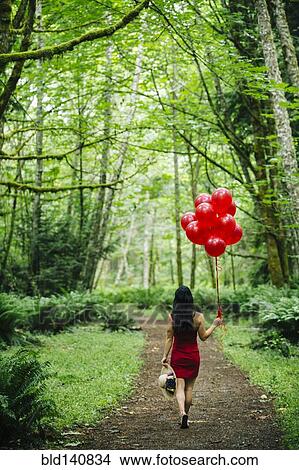Picture - Korean woman holding red balloons in lush forest. Fotosearch