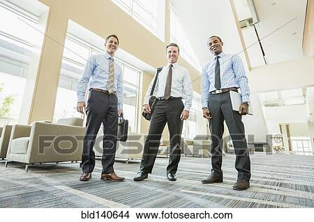 Picture - Low angle view of businessmen smiling in office lobby. Fotosearch