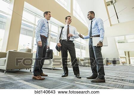 Low angle view of businessmen talking in office lobby View Large Photo Image Stock Image - Low angle view of businessmen talking in office lobby. Fotosearch