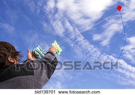 Stock Image - Low angle view of Caucasian man flying kite in blue sky. Fotosearch