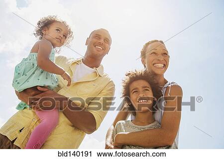 Stock Image - Low angle view of family smiling together outdoors. Fotosearch