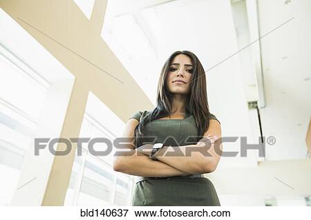 Stock Photo - Low angle view of Hispanic businesswoman standing in office. Fotosearch