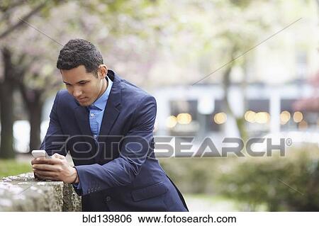 Man in suit using cell phone in urban park View Large Photo Image Stock Photograph - Man in suit using cell phone in urban park. Fotosearch