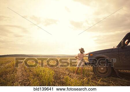 Stock Image - Mari boy leaning on car in rural field. Fotosearch
