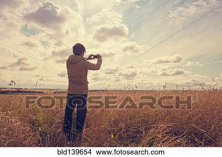 Picture - Mari man photographing rural field with cell phone. Fotosearch