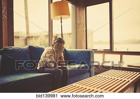 Stock Image - Mixed race boy peeking through fingers in living room. Fotosearch