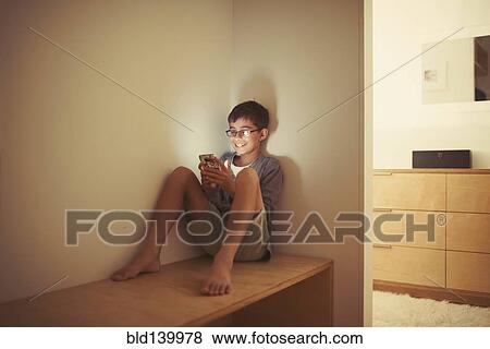 Stock Photo - Mixed race boy using cell phone on bench. Fotosearch