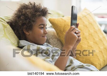Picture - Mixed race boy using digital tablet in living room. Fotosearch