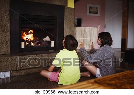 Stock Photograph - Mixed race children relaxing by fireplace in living room. Fotosearch