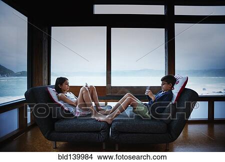 Picture - Mixed race children using cell phones in living room. Fotosearch