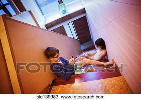 Stock Image - Mixed race children using cell phones on staircase. Fotosearch